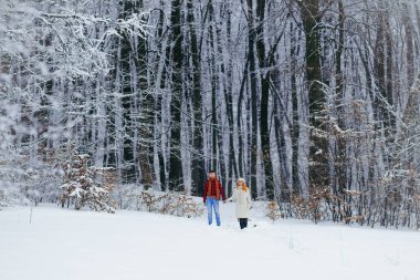 Mutlu sevgi dolu çift elele ve kabarık karlı orman çalışan tam uzunlukta bir kadeh. Noel zamanı.