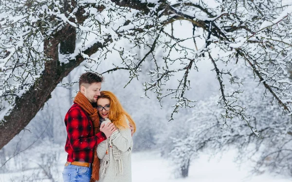 Sensible retrato de media longitud de la atractiva pareja abrazándose durante la nevada en el bosque invernal . —  Fotos de Stock