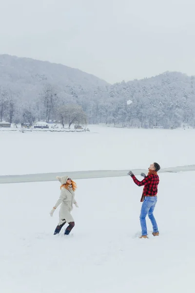 一对相爱的情侣在草地上玩雪球的滑稽漫步, 覆盖着蓬松的雪。圣诞节时间. — 图库照片