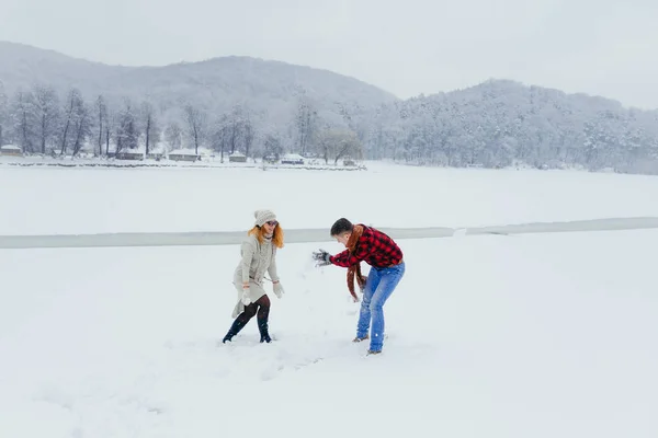 Feliz casal amoroso está jogando bolas de neve um no outro. Localização da floresta de Inverno. Visão horizontal de comprimento total . — Fotografia de Stock