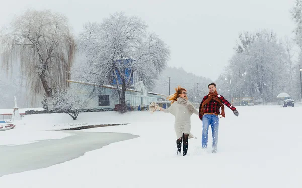Visão completa do alegre casal rindo de mãos dadas durante sua caminhada ao longo da paisagem nevada . — Fotografia de Stock