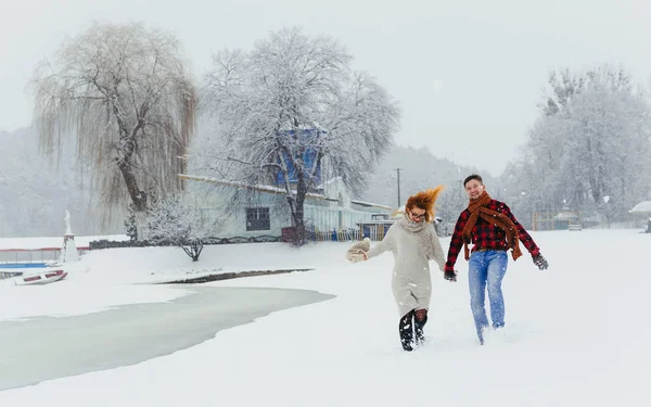 两个快乐的相爱的人牵着手走在白雪皑皑的草地上。户外冬季情侣肖像的乐趣. — 图库照片