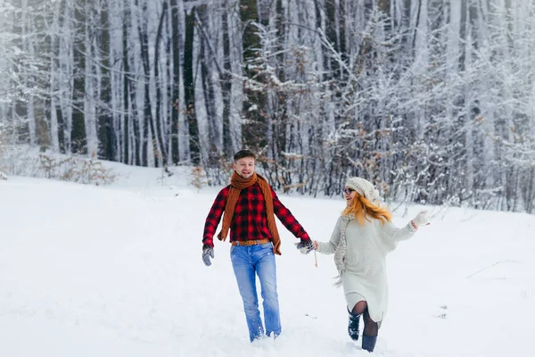 Alegre paseo de la hermosa pareja sonriente tomados de la mano. Localización del bosque nevado. Tiempo de Navidad . — Foto de Stock