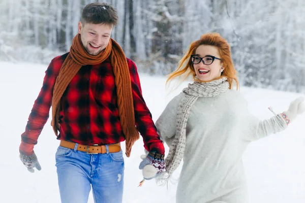 Retrato de cerca de la hermosa pareja alegre cogida de la mano y corriendo por el bosque nevado . — Foto de Stock