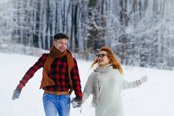 Χριστουγεννιάτικο παραμύθι. Ευτυχισμένο ζευγάρι κρατώντας τα χέρια και χαρωπά τρέχει κατά μήκος στο χιονισμένο δάσος. — Φωτογραφία Αρχείου