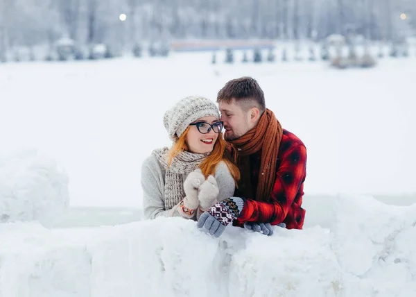 Schönes Porträt des schönen glücklichen Liebespaares, das sich umarmt, während es sich im Winterdorf an die Schneemauer lehnt. — Stockfoto