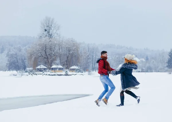 Dois amantes alegres estão de mãos dadas e dançando alegremente na neve no campo. Tempo de Natal . — Fotografia de Stock