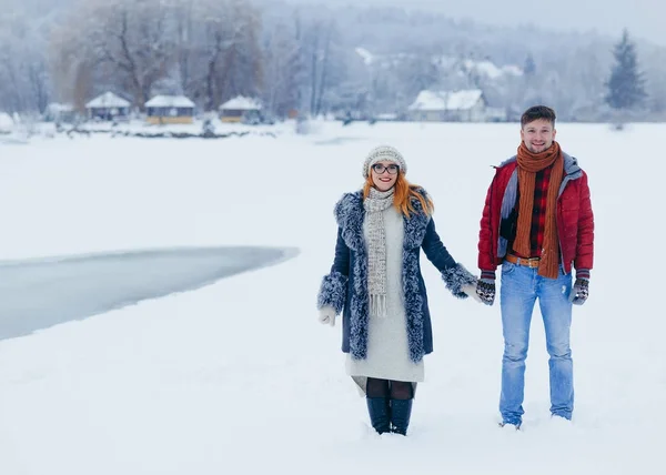 Δύο χαμογελαστά λάτρεις κρατώντας τα χέρια και χαρωπά Μιλώντας κατά τη διάρκεια τους βόλτα στην εξοχή γεμάτο χιόνι. Οριζόντια προβολή. — Φωτογραφία Αρχείου