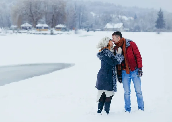 Foto horizontal de larga duración de la adorable pareja joven cogida de la mano y casi besándose en el campo nevado. Tiempo de Navidad . — Foto de Stock