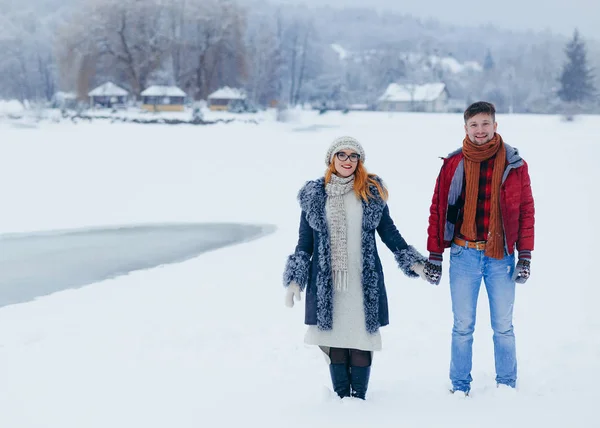 Χαρούμενο ζευγάρι εκμετάλλευση χέρια περπάτημα χιονισμένο χωριό λιβαδιών οριζόντια χιονόπτωσης χαμογελώντας μιλάμε. — Φωτογραφία Αρχείου