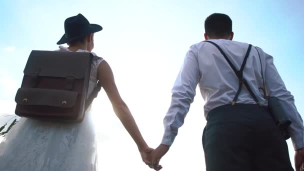 La feliz pareja de recién casados está cogida de la mano y de pie cabeza a cabeza el uno al otro en el fondo del cielo. La vista al alza . — Vídeos de Stock