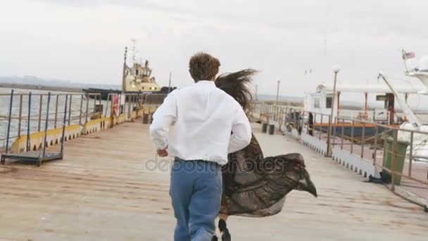 Вид сзади на мужчину, бегущего за женщиной. Обнимающая пара на пирсе . — стоковое видео