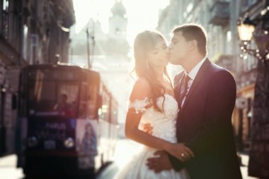 Yakışıklı damat gelin gülümseyen güzel günbatımı sırasında öpüşme yatay portresi. Şehir sokak yerde.