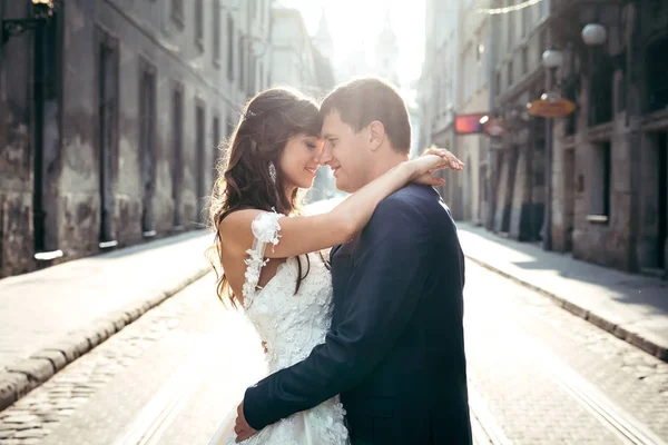 Retrato romántico horizontal de la amorosa pareja recién casada abrazando y tocando las narices en el camino durante la puesta del sol . — Foto de Stock