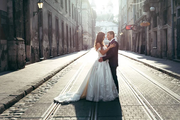 Schönes Hochzeitspaar umarmt sich bei Sonnenuntergang auf der Straße in der Innenstadt. — Stockfoto