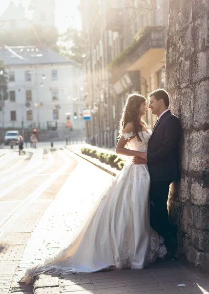 Полнометражный свадебный снимок счастливых объятий молодоженов. Жених опирается на старую каменную стену во время заката . — стоковое фото