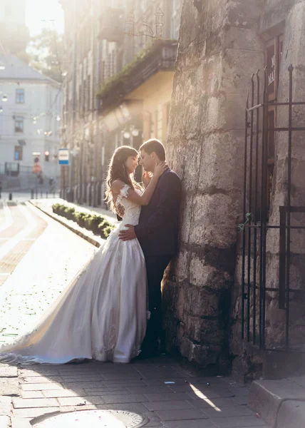 Pełna długość wesele portret piękny szczęśliwy Newlywed para czule przytulanie krzywej ścianie miasta ulicy miasta Lwów zachód słońca. — Zdjęcie stockowe