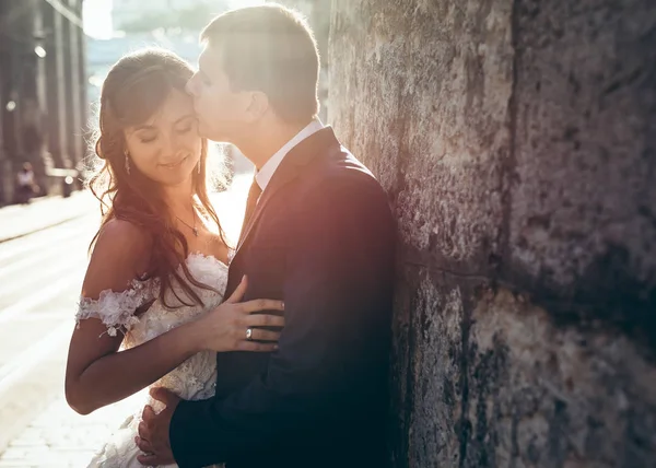 Schöner Bräutigam küsst seine charmante Braut vor dem Hintergrund des Sonnenuntergangs auf die Stirn. Außenporträt. — Stockfoto