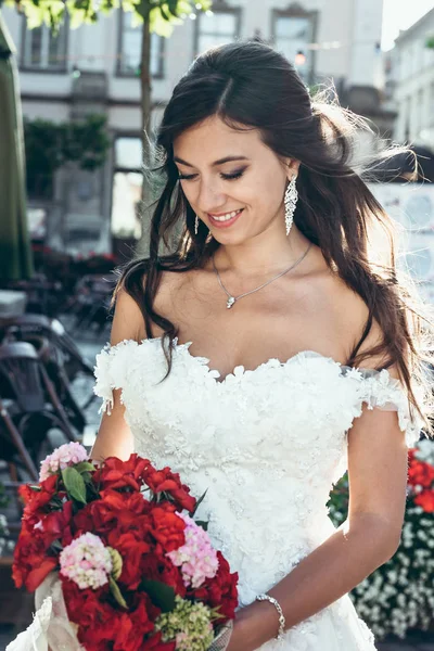 Utomhus porträtt av bedårande brunetter bruden med vackra leende håller bröllop bukett av röda och rosa blommor. — Stockfoto