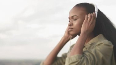 Açık kulaklıklar koyarak ve müzik keyfi çekici sakin Afrikalı kız portresi.