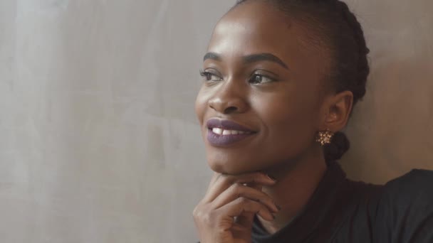 Portret van de mooie Afro-Amerikaanse jonge vrouw met charmante glimlach, mooi gezicht en paarse lipstick op zoek opzij en vervolgens in de camera op de geïsoleerde achtergrond. — Stockvideo