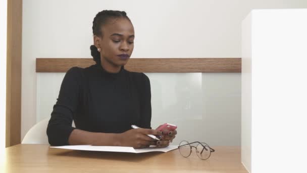 Närbild porträtt av den charmiga afro-american flickan med naturlig make-up i receptionen läsa något på mobiltelefonen och sedan skriva. — Stockvideo