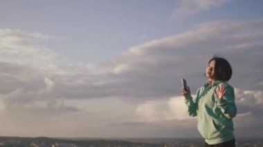 Neşeli genç Asyalı kız güzel gülümseme ile kulaklık ile müzik dinlemek ve gökyüzü arka dans.