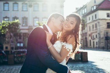 Güneşin gülümseyen güzel esmer gelin boynundan öpmeye yakışıklı damat düğün portre.