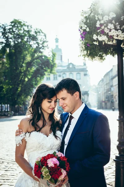 Halvlångt utomhus porträtt av bedårande elegant bröllopsparet mjukt kramas, ständiga head-to-head och hålla buketten av röda och rosa blommor. — Stockfoto