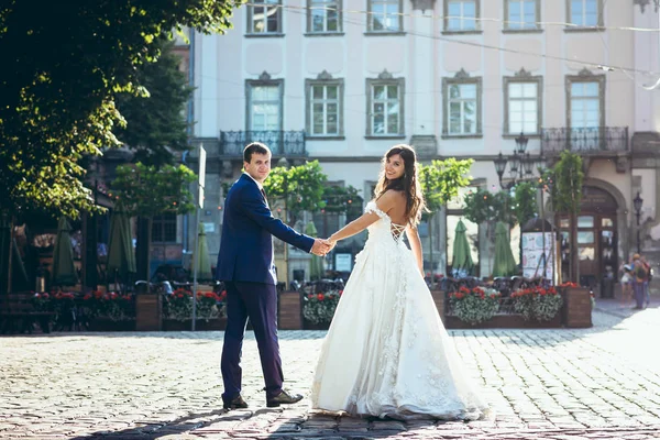 Hátulnézet a vidám imádnivaló newlywed pár kézen az utcán, a háttérben a gyönyörű ház. — Stock Fotó
