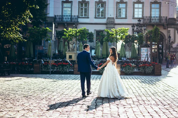 Happy newlyweds are holding hands during the walk along the town street during the sunny day. — Stock Photo, Image