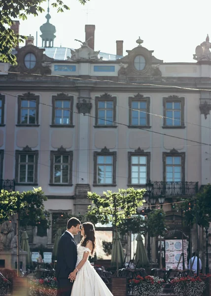 Belo retrato romântico dos recém-casados felizes de mãos dadas e narizes carinhosos tocando no fundo da velha casa coberta de plantas . — Fotografia de Stock
