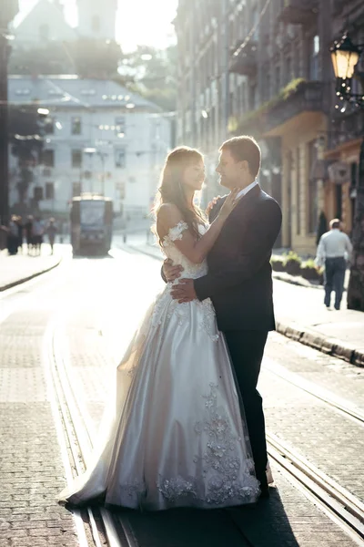 Hermosa sonrisa pareja recién casada se abraza tiernamente en la calle de la ciudad durante el atardecer . — Foto de Stock