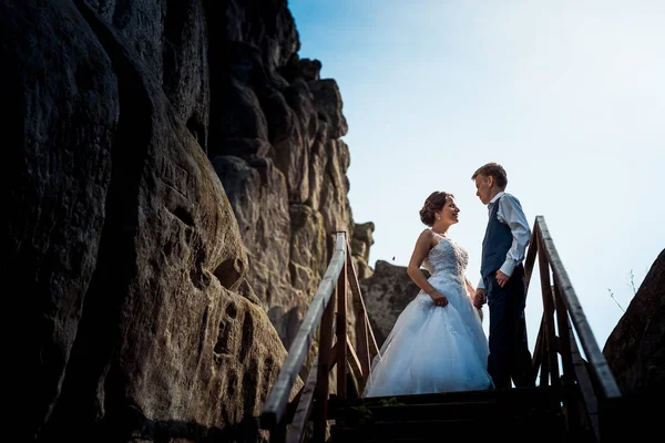 Romantik rock yakınındaki ahşap merdivenler yakınındaki elele güzel gülümseyen yeni evliler portresi. — Stok fotoğraf