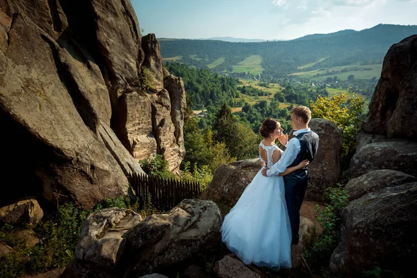 Acima do retrato romântico dos recém-casados. O belo noivo acariciando suavemente a bochecha da noiva enquanto estava nas montanhas no fundo da bela paisagem de florestas e campos . — Fotografia de Stock