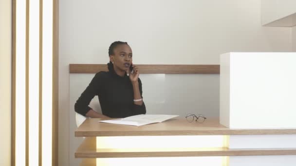 Afro-american dívka na recepci mluví přes mobilní telefon a něco v podobě vyplnění. Umístění kanceláře. — Stock video