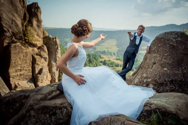 Yeni evli çift ayrı ve birbirlerine yardım eder. Damat kayaya yaslanmış iken gelini uzun elbiseli taş üzerine oturuyor. Güzel doğa görünümü. — Stok fotoğraf