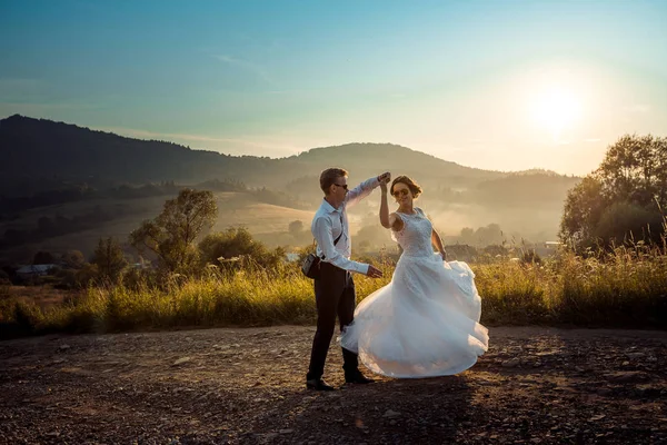 Συναισθηματικά γάμου πυροβολισμό στο νεόνυμφο ζευγάρι ευτυχισμένο αίγλη χορεύοντας στο δρόμο κατά το ηλιοβασίλεμα. Όμορφη φύση προβολή. — Φωτογραφία Αρχείου