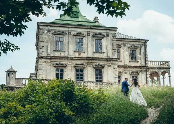 Der Bräutigam führt die hinreißende Braut an der Hand auf dem Weg zum alten Haus. schöne Aussicht auf die Landschaft. — Stockfoto
