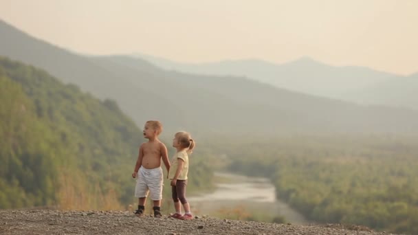 Ein kleines Mädchen im Alter von 4 Jahren hält die Hand und küsst den Jungen, während er während des Sonnenuntergangs auf den Bergen steht. Drohnen-Ansicht. — Stockvideo