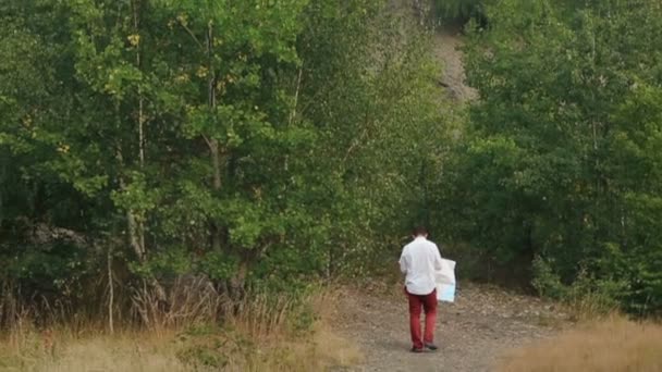 La vue arrière du touriste errant avec la carte le long de la forêt dans les montagnes. La vue de drone sur le beau paysage . — Video