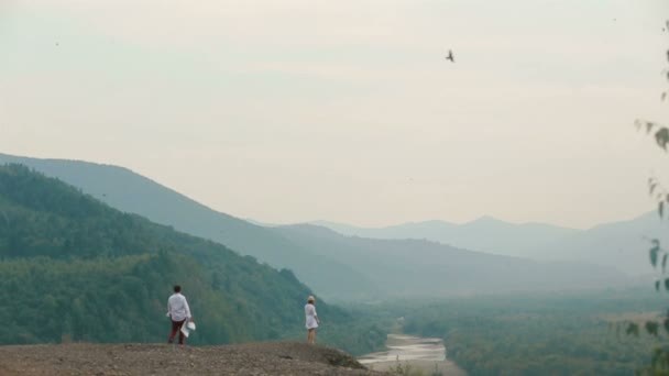 Вид сзади путешественника с картой на красивую блондинку, стоящую на краю гор и наслаждающуюся пейзажем . — стоковое видео
