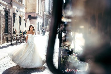 Güzel gelin güzel gülümseme ile güneşli sokağın ortasında yuvarlak dönüyor. Tam uzunlukta yatay dikey.