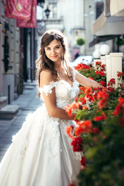 Очаровательная молодая брюнетка невеста улыбается и позирует на улице возле красных цветов — стоковое фото