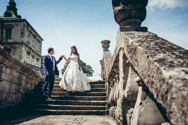 Ganzes Hochzeitsportrait des entzückenden Brautpaares, das die alte Burgstraße hinuntergeht. Der Bräutigam hilft seiner Geliebten mit der Hand. — Stockfoto