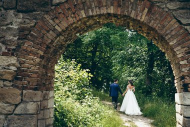Eski taş kemer elele ve yeşil orman yolu boyunca yürüyüş şık yeni evli çift bakın.