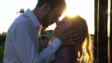 Yakışıklı genç şefkatle sevgilisi yüzünü dokunaklı ve günbatımı sırasında onu öpüyor. Yakın çekim duyarlı portre.