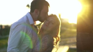 Genç esmer adam çekici sarışın sevgilisine güneşin arka plan başında öpüyor. Açık portre.