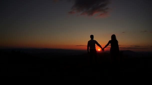 カップルのシルエットのロマンチックな屋外の肖像画は、夕日の間に抱き合ってキスをします。美しい風景。女が花束を持ってる. — ストック動画