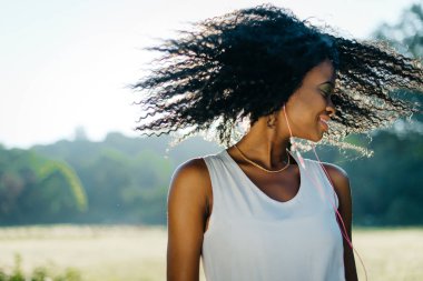 Doğal makyaj ile oldukça mutlu Afrikalı kız uzun kıvırcık saçları sallayarak ve onun kulaklık açık müzik keyfi.